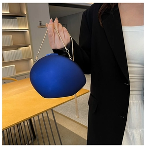 Blue oval shell clutch bag with gold snake handle shown by a model in a modern office