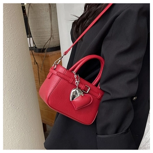 Detail view of red pebble leather handbag with silver heart charm and strap on black suit