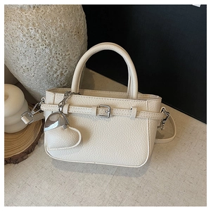 Detail of cream white leather handbag featuring textured litchi grain and heart pendant