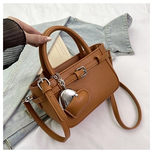 Brown lychee grain handbag with adjustable strap and heart charm on a denim background