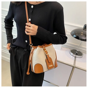 Detail of canvas bucket bag with brown leather trim and golden metal buckle closure