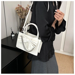 White mini tote bag with large bow and pearl chain shown on model in modern setting