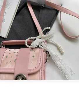 Close-up of pink leather crossbody bag with sparkling rhinestones and pearl bow detail