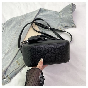 Detail shot of black pebbled leather texture on a compact crossbody bag with silver hardware