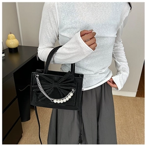 Close-up of black crossbody bag featuring a large bow and pearl-accented silver chain