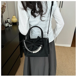 Close-up of black crossbody bag with velvet bow and elegant pearl chain strap detail