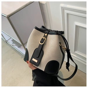 Detail of canvas bucket bag showing beige fabric texture and black leather trim accents