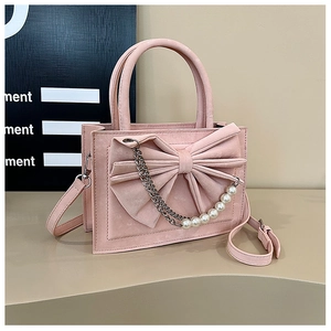 Close-up of pink suede bag featuring a 3D bow, white pearl accents, and metal chain strap
