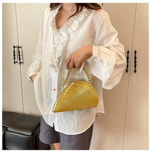 Detail of golden shell-shaped acrylic clutch with beaded handle and fine chain strap