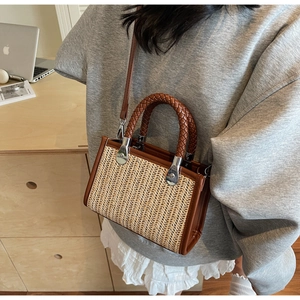 Close-up of handwoven straw handbag featuring brown leather trim and metallic buckle detail