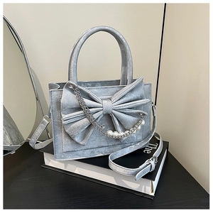 Silver leather shoulder bag featuring a large bow and pearl chain detail on a book