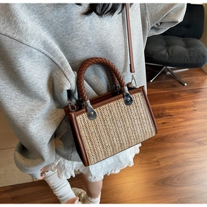 Detail of woven straw tote with brown leather trim and sturdy braided top handle