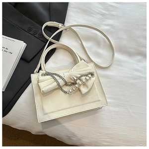 Detail of cream crossbody bag with large bow, pearl chain and elegant leather texture