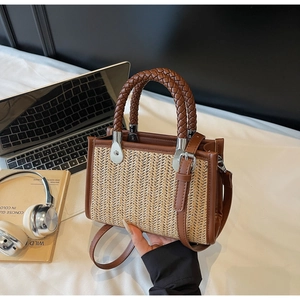 Detail of woven straw mini tote bag with brown leather trim and metallic handle rings