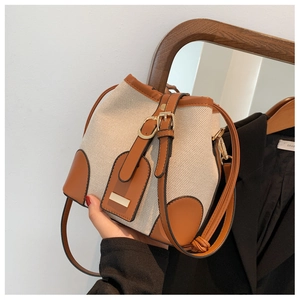 Detail of canvas bucket bag with brown leather trim and metal buckle on adjustable strap