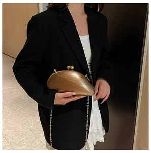 Detail of shell-shaped marble clutch featuring gold orb clasp and chain strap on a model
