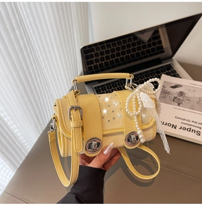 Detail of yellow baguette bag with rhinestone decor, pearl chain and lace bow