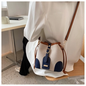 Chic canvas bucket bag with contrast leather trim shown as a crossbody on a model