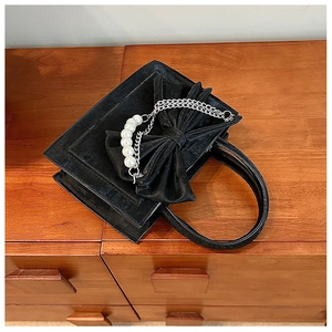 Detail of black velvet handbag featuring a large bow and white pearl chain handle
