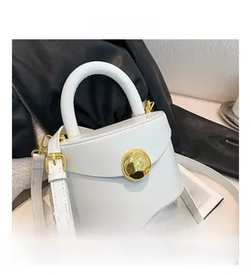 Close-up of a white leather bag featuring a gold spherical clasp and textured strap