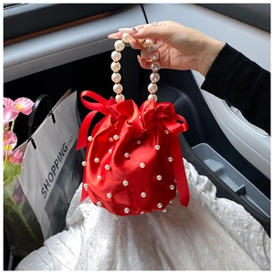 Detail of red satin bucket bag with pearl handle and silk bow decoration in a car