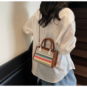 Detail view of colorful striped knit shoulder bag with brown leather trim and silver hardware