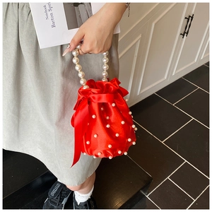 Detail of red satin bucket bag with pearl handle, bow decoration and white pearl accents
