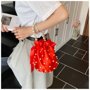 Detail of red satin drawstring bucket bag with pearl handle and ribbon bow accents