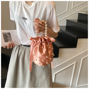 Detailed view of pink satin bucket bag with pearl handle and silk ribbon bow accent