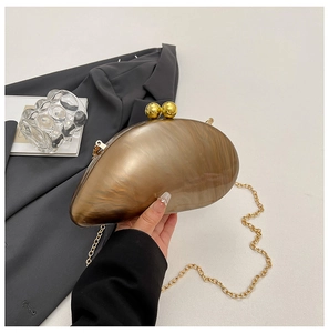 Macro detail of marble-textured shell clutch bag with gold sphere clasp and chain