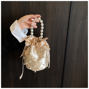 Detail of champagne satin bucket bag with pearl embellishments and silk ribbons