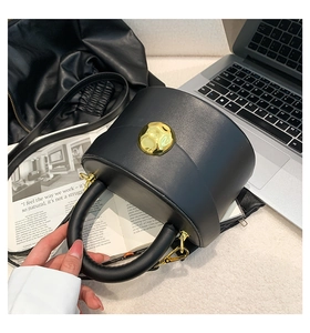 Detail of a black leather cylindrical handbag with a gold hammered metal buckle