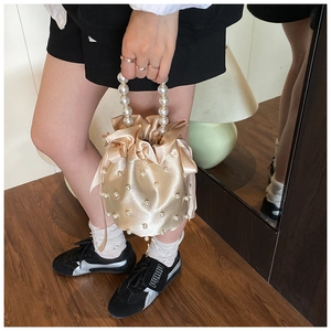 Detail of satin bucket bag featuring pearl top handle and elegant side ribbon bows
