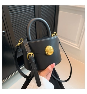 Detail of a minimalist black leather semi-circle handbag with golden buckle held by a model
