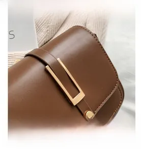 Detail of a brown leather shoulder bag featuring a modern matte gold U-shaped buckle