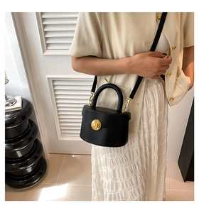 Close-up of black matte leather bag featuring a large circular gold buckle and strap