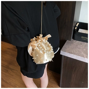 Champagne satin bucket bag with pearl embellishments and a gold chain strap worn by a model