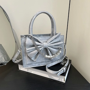 Silver metallic square handbag with large bow, pearl chain and top handle on books