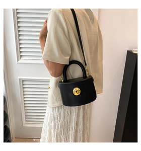 Detail of a structured black leather handbag with a prominent round gold buckle and handle