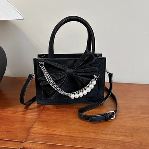 Elegant black velvet handbag with large bow and pearl chain strap, shown on a wooden table