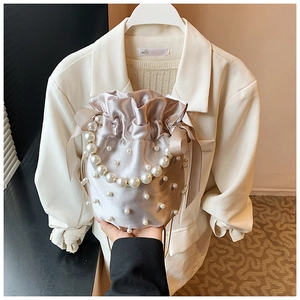 Detail of champagne satin bucket bag with elegant pearls and silk ribbon bow accent