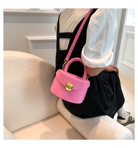 Close-up of a pink leather crossbody bag with a large gold circular buckle detail