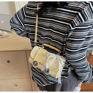 Detail of light yellow pillow bag with lace trim, pearls and silver rivets on a desk