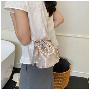Detail of champagne satin bucket bag with pearls and ribbon on a female model