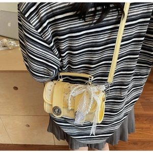 Detail of yellow cylinder crossbody bag with pearl lace bow in cozy study setting