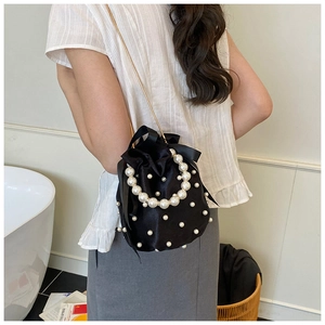 Detail of black satin bucket bag with pearl handle and golden chain on a white background