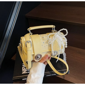 Detail of cream yellow leather bag with rhinestone flap, pearl bow, and lace charms