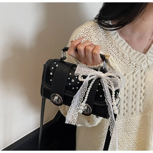 Detail of black leather handbag featuring a white lace bow and elegant pearl tassel