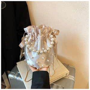 Detail of champagne satin bucket bag with pearl embellishments and a ribbon bow