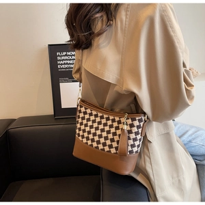 Detail view of checkered bucket bag with brown leather base and stylish tassel charm